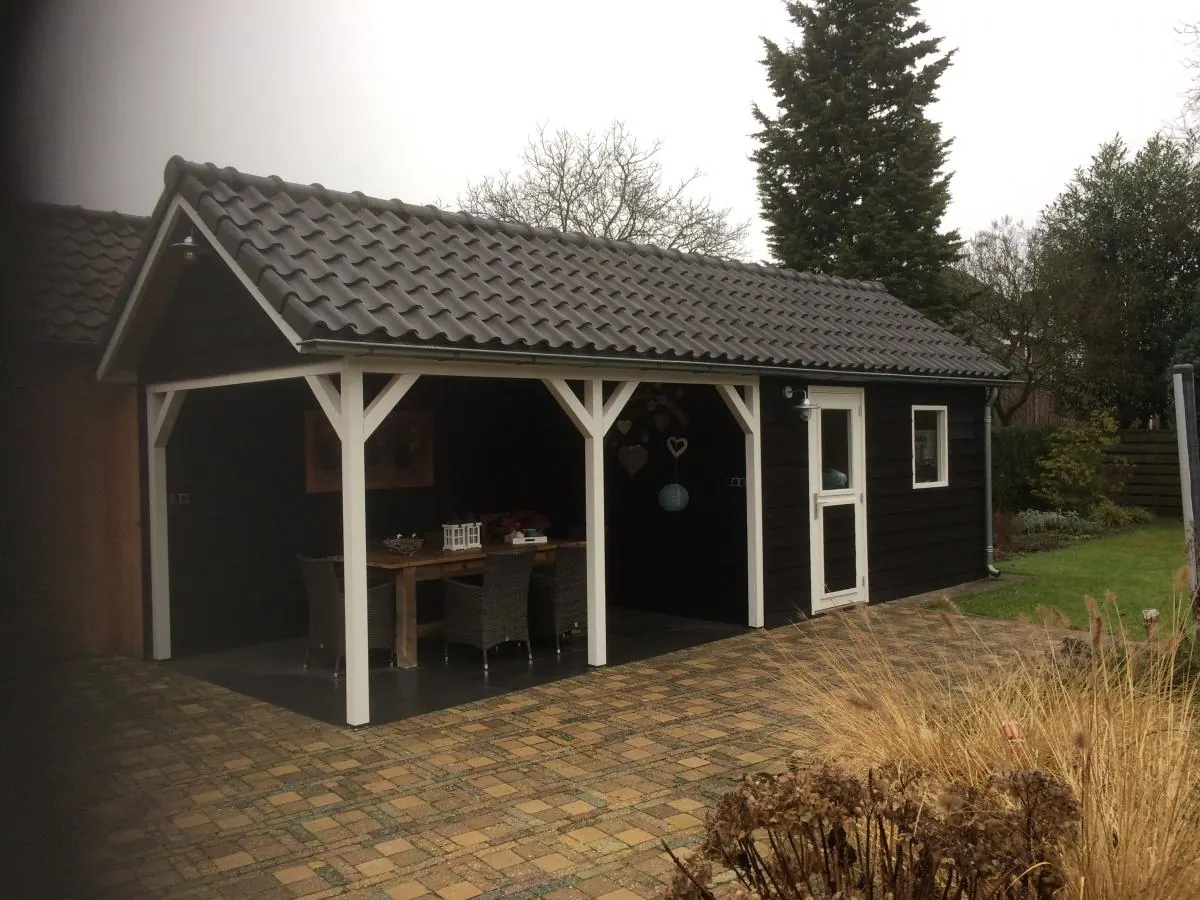 Zwarte houten schuur met overkapping en pannendak
